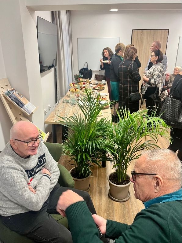 dwóch siedzących panów podczas rozmowy, w tle inni ludzie