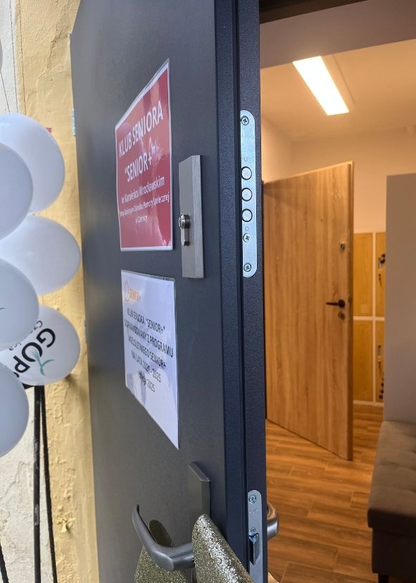 zdjęcie przedstawiające uchylone drzwi do klubu, obok balony z napisem GOPS Czernica